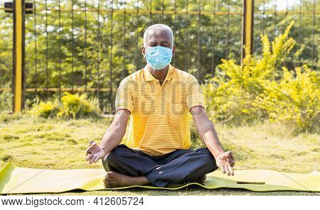 Senior Man In Medical Face Mask Meditating On Yoga Mat At Park - Cconcept Of Elderly People Healthca