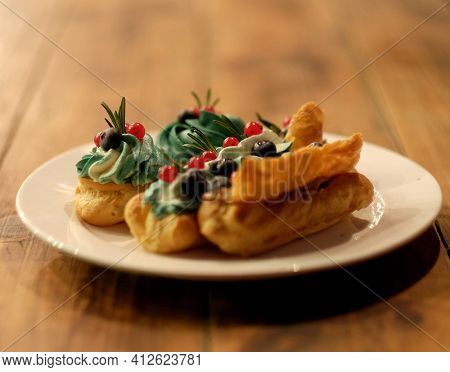 Tasty French eclairs with icing, cream, fresh berries and sugar decor elements. Set of delicious eclairs with creative colorful decor on white plates on neutral textured table. Homemade profiteroles