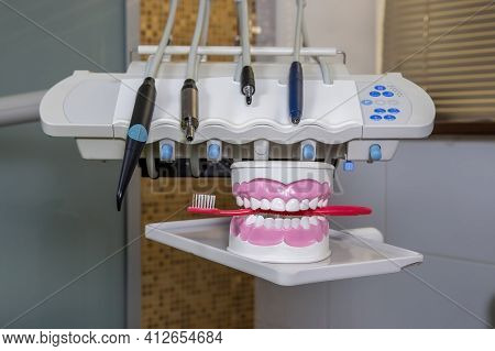 Clean Teeth Dental Jaw Model And Red Thooth Brush On The Table In Dentist's Office. The Concept Of P