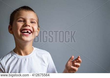 Boy Without Milk Upper Tooth In White T-shirt Smiling On The Gray Background.