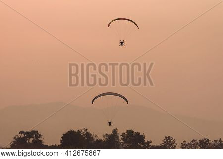 Silhouette Of The Paramotor Gliding And Flying In The Air Through Soft Sunlight Sky.