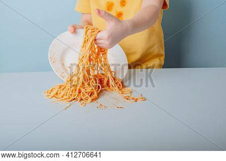 Dropped A Plate Of Spaghetti On The Table. Children's Hands Collect Pasta. Concept Of Dirty Stains O