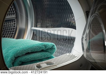 Closeup View Of A Clothes Dryer With Turquoise Towels Inside And An Open Door. Washing Machine In A 