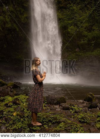 Young Caucasian Woman Spending Time Near Waterfall. Meditation And Relaxation. Hands In Namaste Mudr