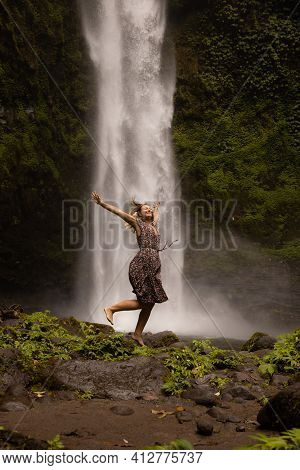 Happy Caucasian Woman Jumping Near The Waterfall. Legs In Motion Movement. Nature And Environment Co