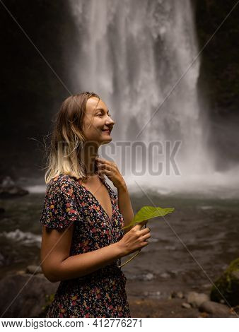 Caucasian Woman Holding Leaf, Enjoying Waterfall Landscape. Nature And Environment Concept. Travel L