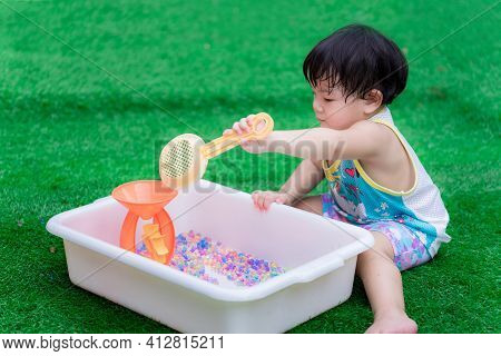 Asian Preschool Baby Uses An Orange Toy Sieve To Scoop Rainbow Beads And Play With Water Cone That I