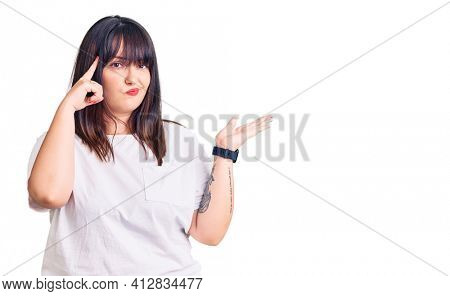 Young plus size woman wearing casual clothes confused and annoyed with open palm showing copy space and pointing finger to forehead. think about it. 