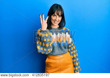 Young hispanic woman wearing casual winter sweater showing and pointing up with fingers number three while smiling confident and happy. 