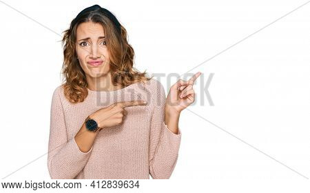 Beautiful young caucasian woman wearing casual sweater pointing aside worried and nervous with both hands, concerned and surprised expression 