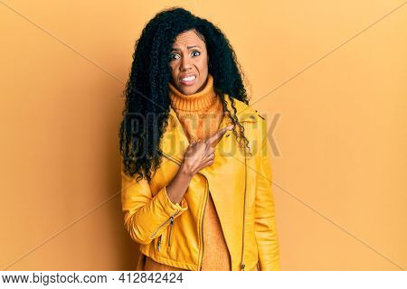 Middle age african american woman wearing wool winter sweater and leather jacket pointing aside worried and nervous with forefinger, concerned and surprised expression 