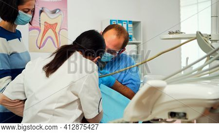 Stomatologist With Face Mask And Gloves Using Drill Tool For Cleaning Teeth Of Little Patient Workin