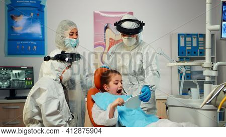 Happy Little Girl In Ppe Suit Looking In The Mirror After Dental Intervention Sitting In New Normal 