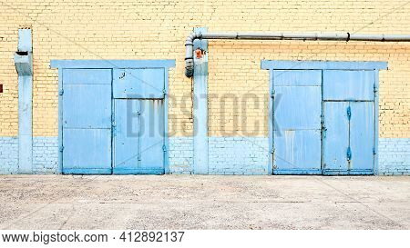 Cityscape. Urban Symmetric View Of Abandoned Factory Building Blue Painted Two Rusty Gates On Yellow