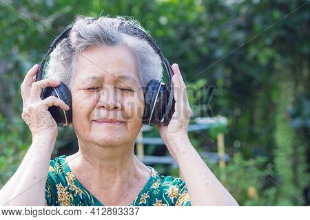 Senior Woman With Short Gray Hair Wearing Wireless Headphones Listening To A Favorite Song, Smiling 