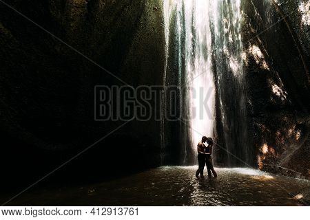 Beautiful Couple In A Cave With A Waterfall. Athletic Man And Woman Under The Streams Of A Waterfall