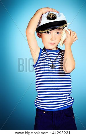 Küçük gülümseyen denizci çocuk deniz kabuğu sesini dinliyor.