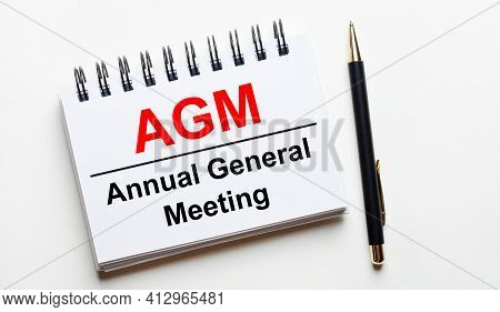On A Light Background, A White Notebook With Are Words Agm Annual General Meeting And A Pen.
