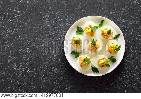 Deviled Stuffed Eggs With Egg Yolk, Bacon, Mustard And Parsley On Dark Stone Background With Copy Sp