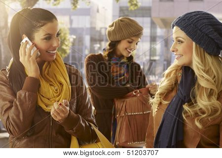 Three girls outdoors, talking on mobile, chatting. Friendship.