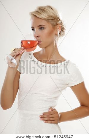 Portrait of happy smiling young attractive blonde woman with glass of red rose wine, in white dress isolated on white background