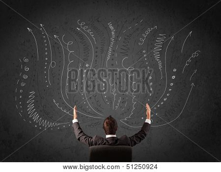 Thoughtful young businessman sitting and deciding in front of a chalkboard with sketched arrows and lines in different directions