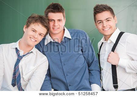 Three happy students in nice shirts standing in front of a school chalkboard