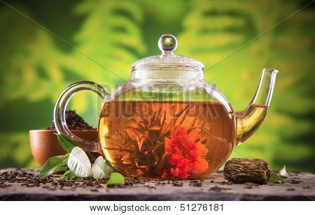 Teapot with blooming tea on blur green background