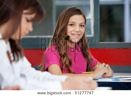 Portrait of teenage schoolgirl sitting with female friend in foreground at classroom