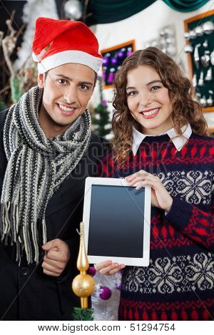 Portrait of happy young couple showing digital tablet while standing at Christmas tore