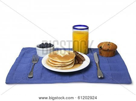 Breakfast still life with glass of orange juice, blueberries, pancakes, sausage, muffin, on blue place mat with white background