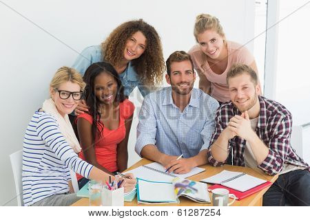 Team of happy young designers having a meeting smiling at camera in creative office