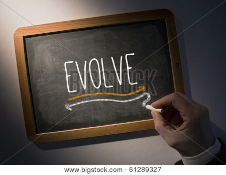 Hand writing the word evolve on black chalkboard
