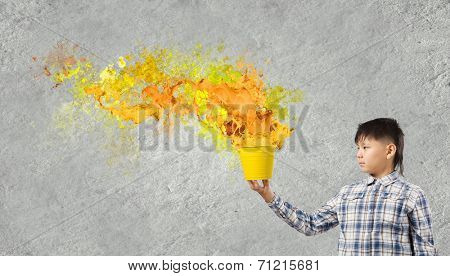 Young boy splashing colorful paint from bucket