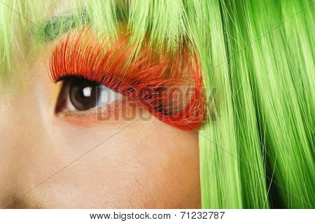 Extreme close-up of young woman's face with false eyelashes and green wig