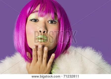Portrait of young funky woman in pink wig blowing kiss over purple background