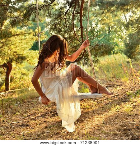 Young woman is swinging on a swing in summer pine forest. Image toned and noise added.