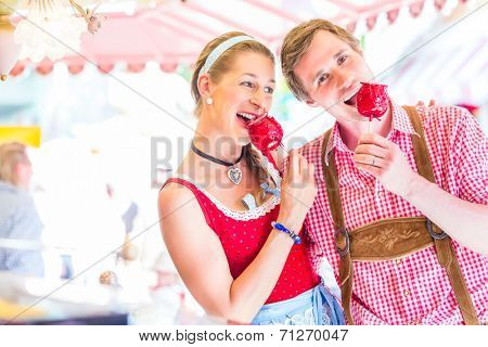 Couple visiting together Bavarian fair in national costume eating  candy apple