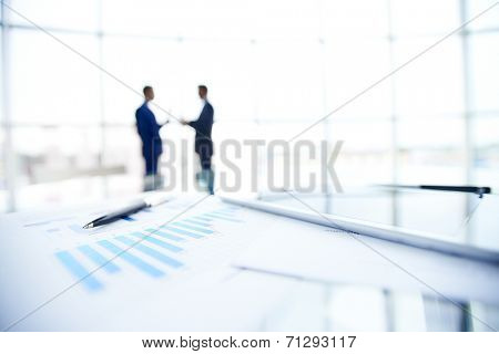 Business documents and pen at workplace on background of businessmen interacting