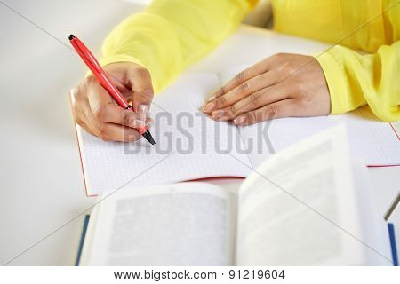 people and education concept - close up of fafrican american female hands with book writing to notebook at school