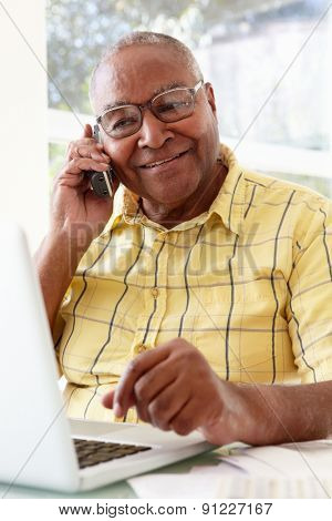 Senior Man On Phone Using Laptop At Home