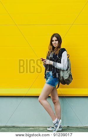 Happy young girl listening music  in headphones over yellowwall
