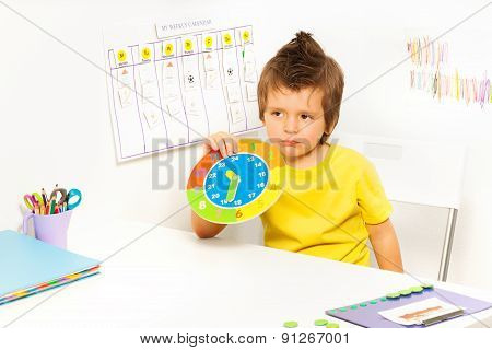 Boy holding carton clock sitting at the table