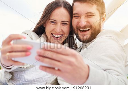 outdoor photo of happy laughing couple taking a selfie and looking at cellphone