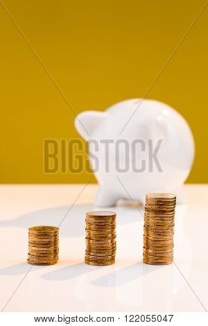 White piggy bank with a stack of coins and a yellow background