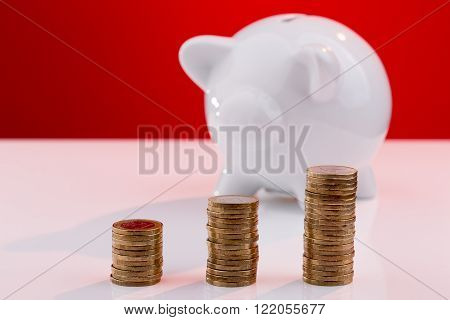 White piggy bank with a stack of coins and a red background