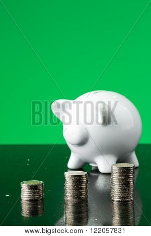 White piggy bank with a stack of coins and a green background