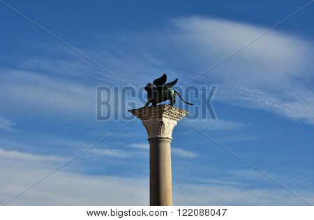 Bronze statue of Saint Mark winged lion among clouds at the top of an ancient column in Venice