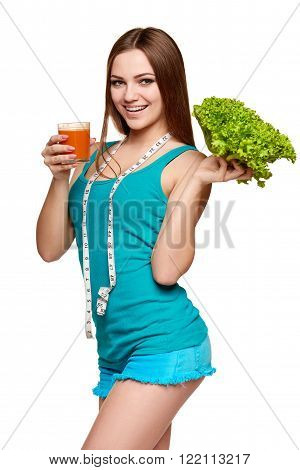 Dieting, slimming, detox cocktail. Happy girl holding a glass of carrot juice and fresh lettuce, with measurement tape over her neck, over white background