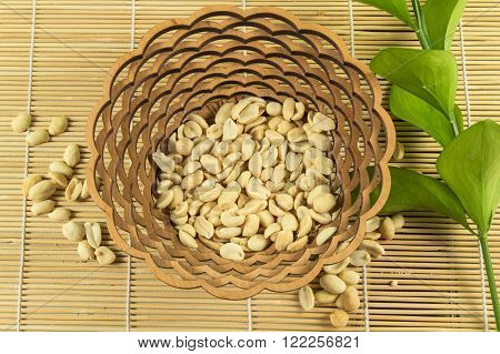 Salted peanuts in a beautiful wooden bowl on a bamboo Mat with green branches of ruskus.